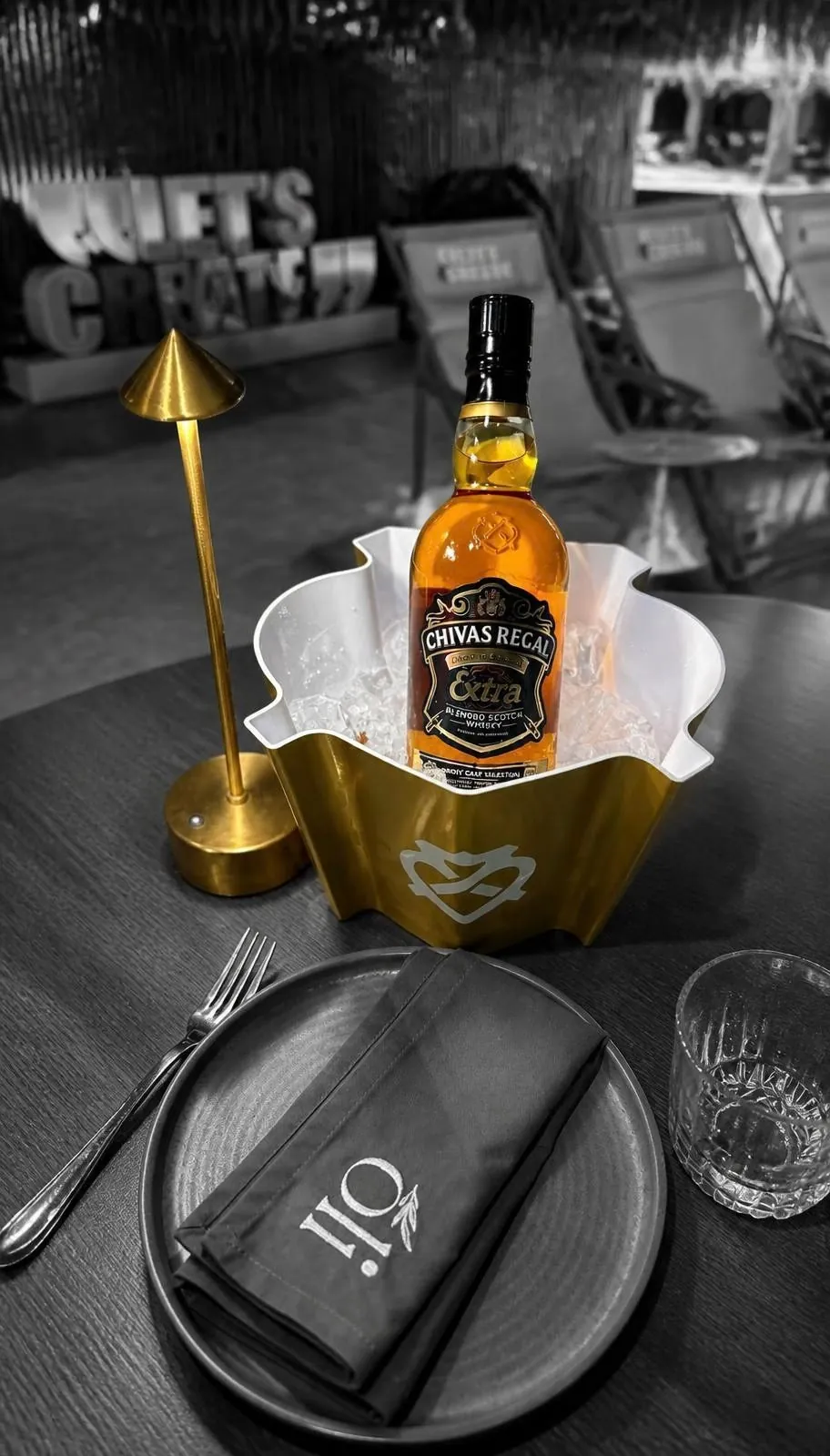 Gespritzter Eiskübel mit gewelltem Rand und einer Whiskyflasche, auf einem gedeckten Restauranttisch.