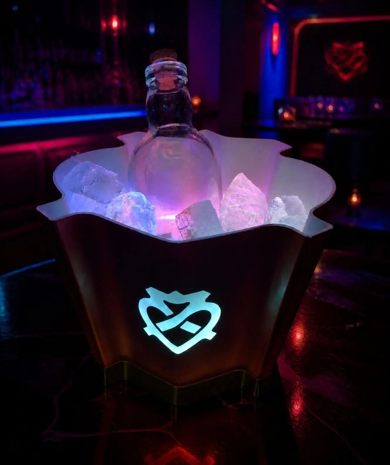 Beleuchteter gespritzter Eiskübel, weiß-blau leuchtend, mit einer Flasche im Eis, fotografiert in einem Club.