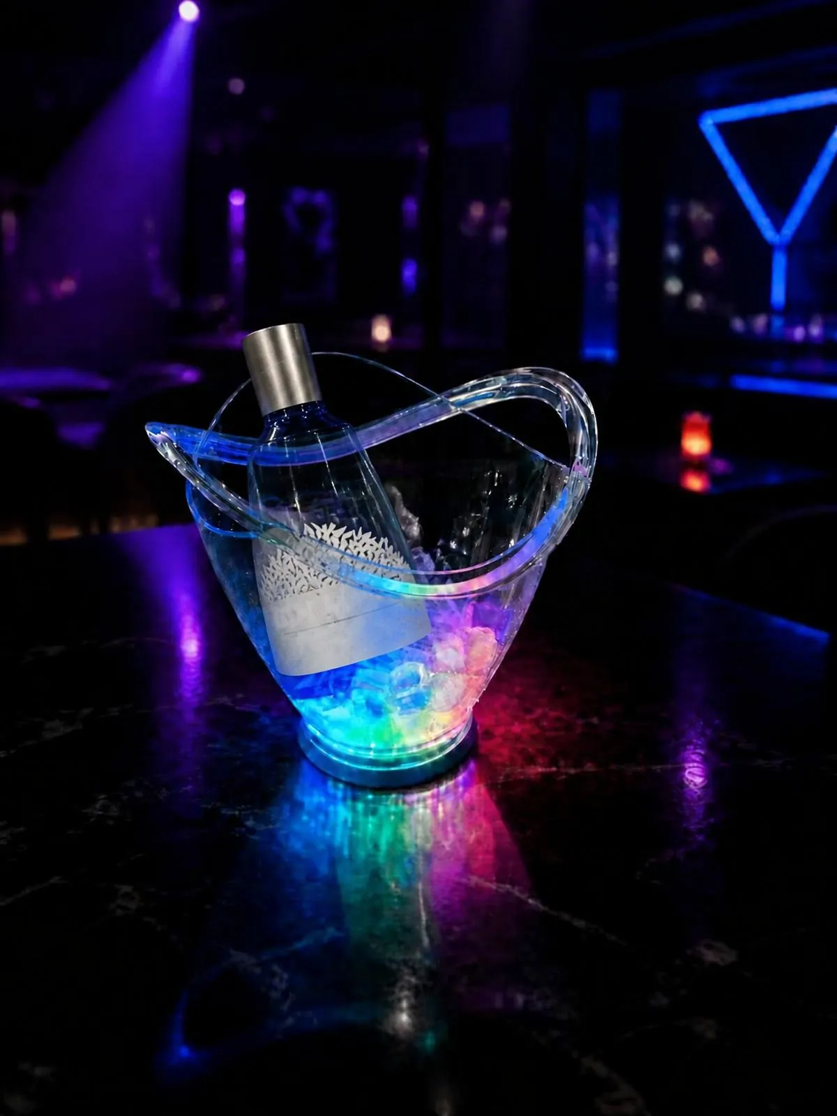 Transparenter gespritzter Eiskübel, von innen beleuchtet, gefüllt mit Eis und einer Flasche, auf dunkler Bartheke.