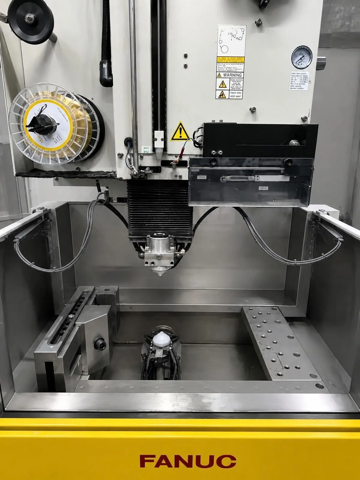 Fanuc-Bearbeitungszentrum mit geöffnetem Arbeitsraum, Werkzeugspindel darüber und Spannvorrichtung auf dem Tisch.