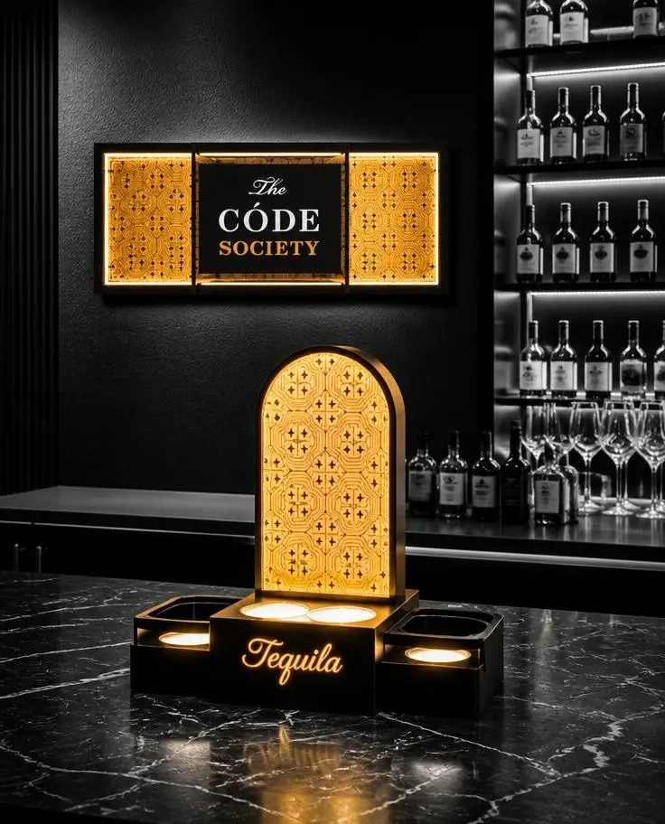 Arched backlit display with a perforated gold face and a brand header, set on a dark marble bar floor.