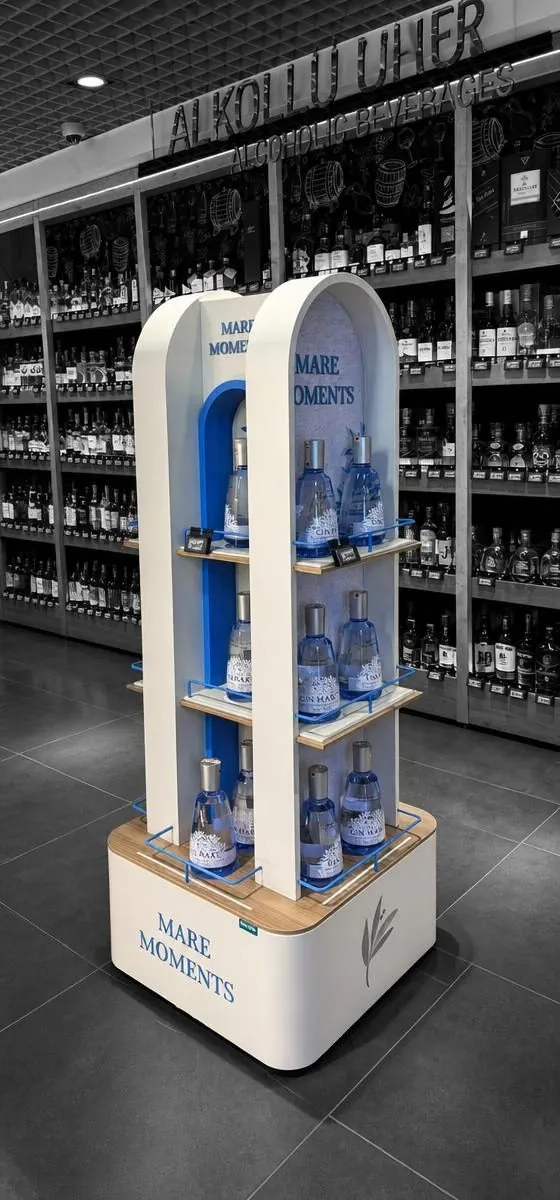 Freestanding arch-shaped tower in white and light oak with lit shelves of spirits, standing in a store aisle.