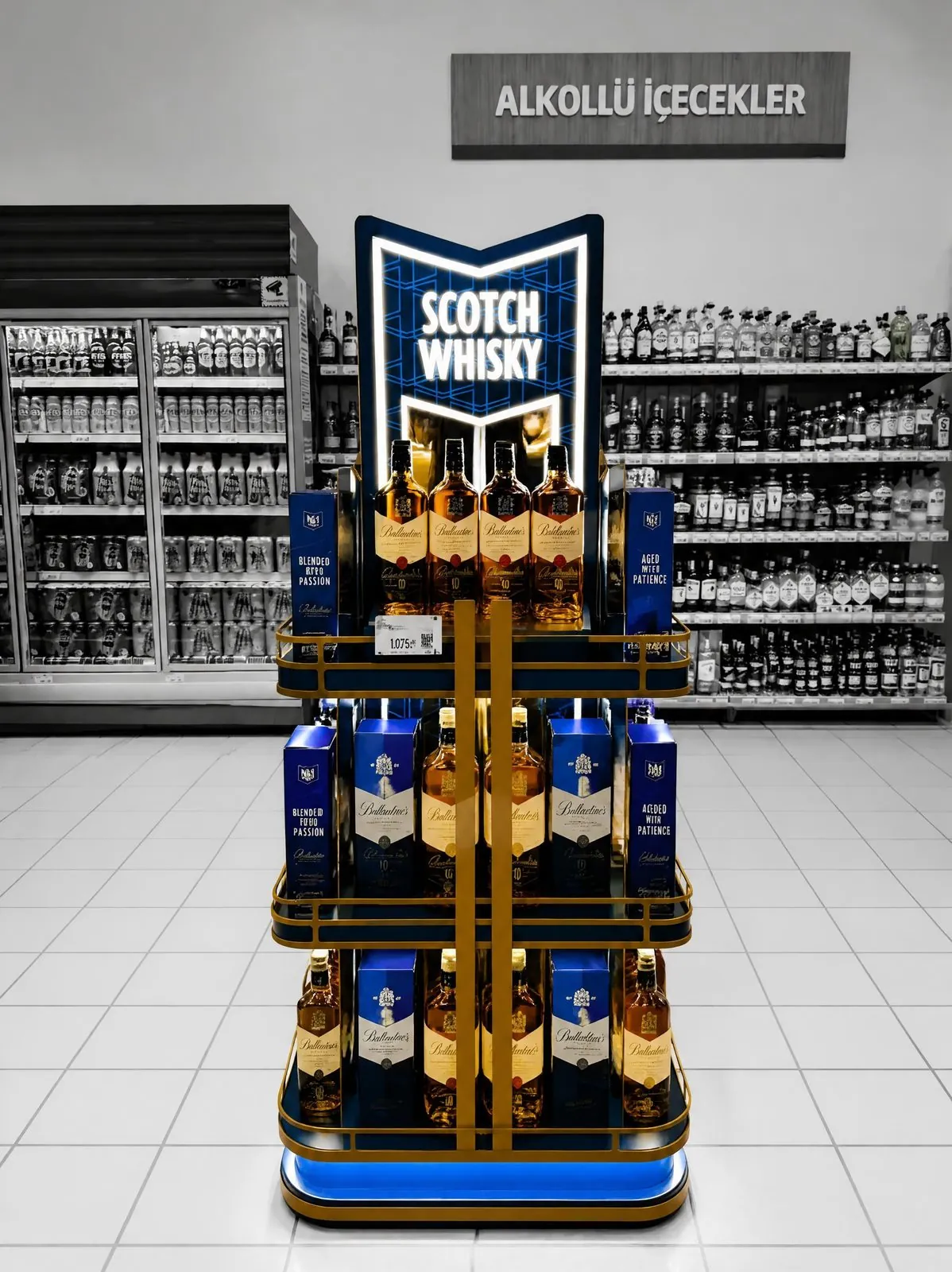 Blue and gold island display under a ceiling sign reading "Alkollü İçecekler", stocked with spirits on several levels.