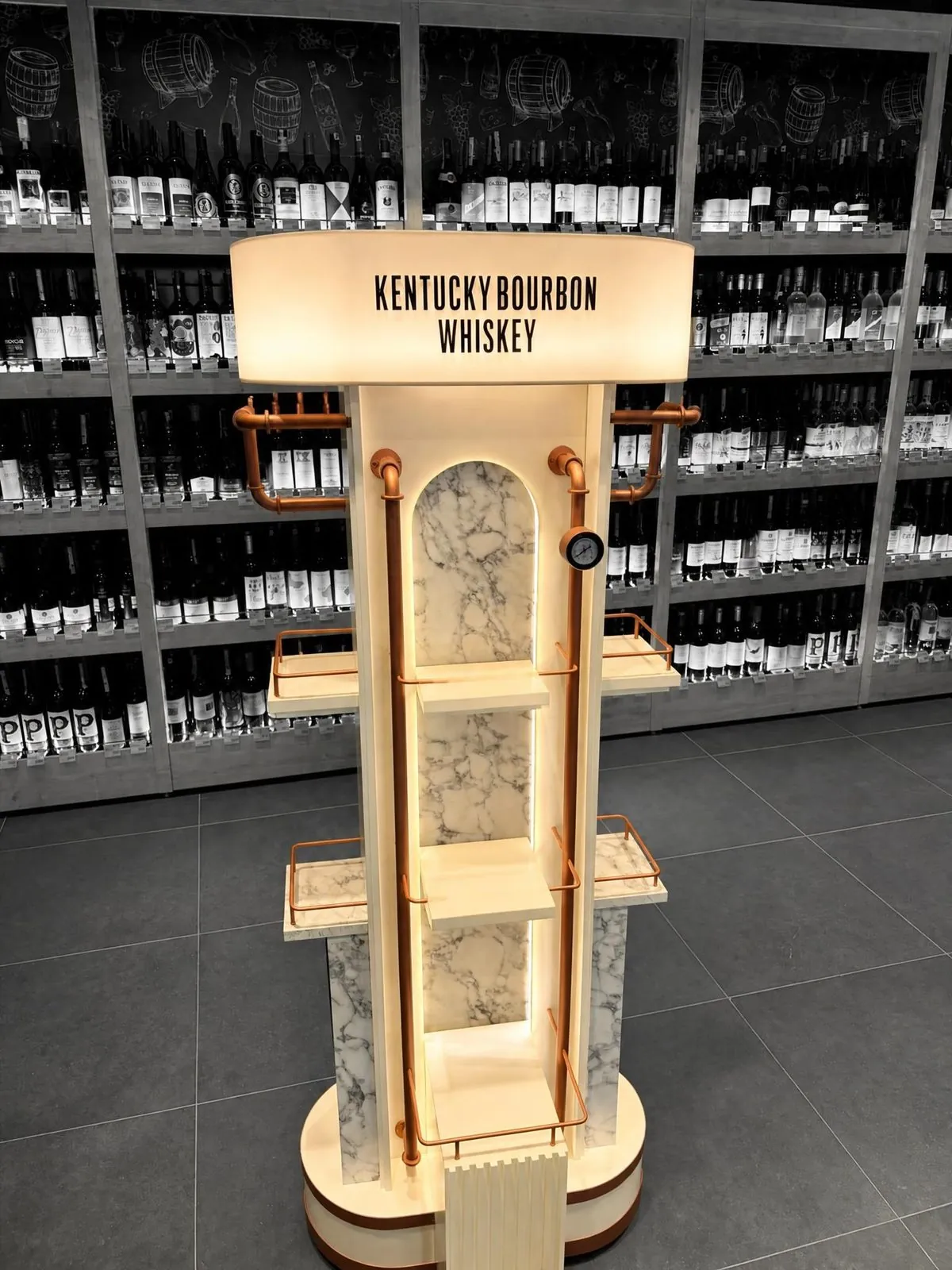 Display in Creme- und Marmoroptik mit einem Marken-Kopfschild und beleuchteten Böden im Spirituosengang.
